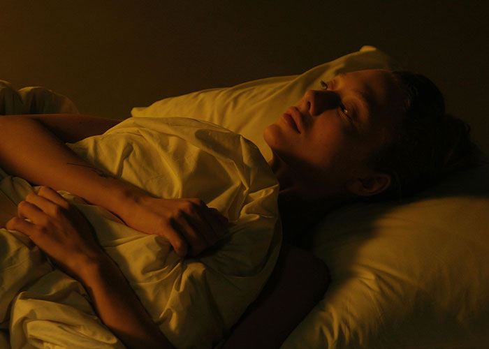 Person lying awake in bed at night, reflecting on bizarre family behaviors considered normal by many families.