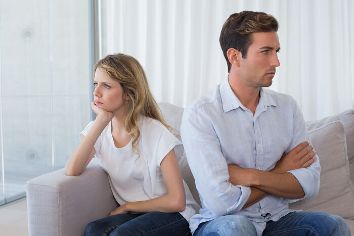 Couple sitting apart on couch looking upset and distant, showing signs of relationship trouble and days being numbered.