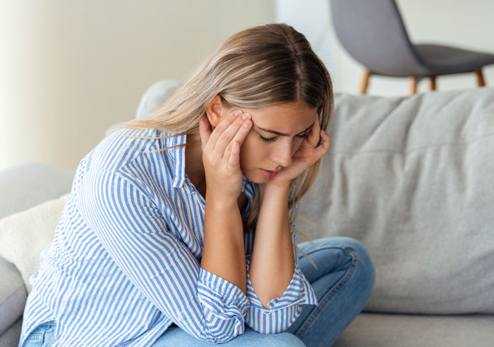 Woman sitting on couch with hands on face, appearing worried while using a mil-tracking-app-son indoors. Woman sitting on couch with hands on face, appearing worried while using a mil-tracking-app-son indoors.