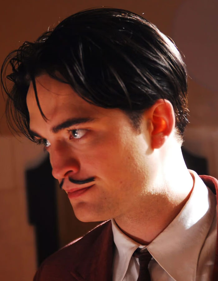 Young man with dark hair and mustache in a brown suit, portraying a scene related to Robert Pattinson Twilight intimate scene. Young man with dark hair and mustache in a brown suit, portraying a scene related to Robert Pattinson Twilight intimate scene.