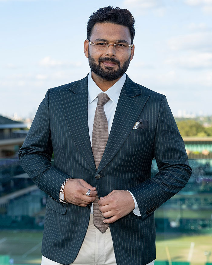 Man in pinstripe suit and glasses posing outdoors with tennis courts in the background at a Wimbledon event. Man in pinstripe suit and glasses posing outdoors with tennis courts in the background at a Wimbledon event.