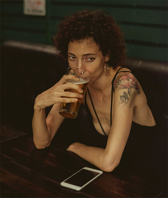 Woman with tattoo drinking beer at a bar looking thoughtful about guy's female best friend and surprise birthday party conflict Woman with tattoo drinking beer at a bar looking thoughtful about guy's female best friend and surprise birthday party conflict