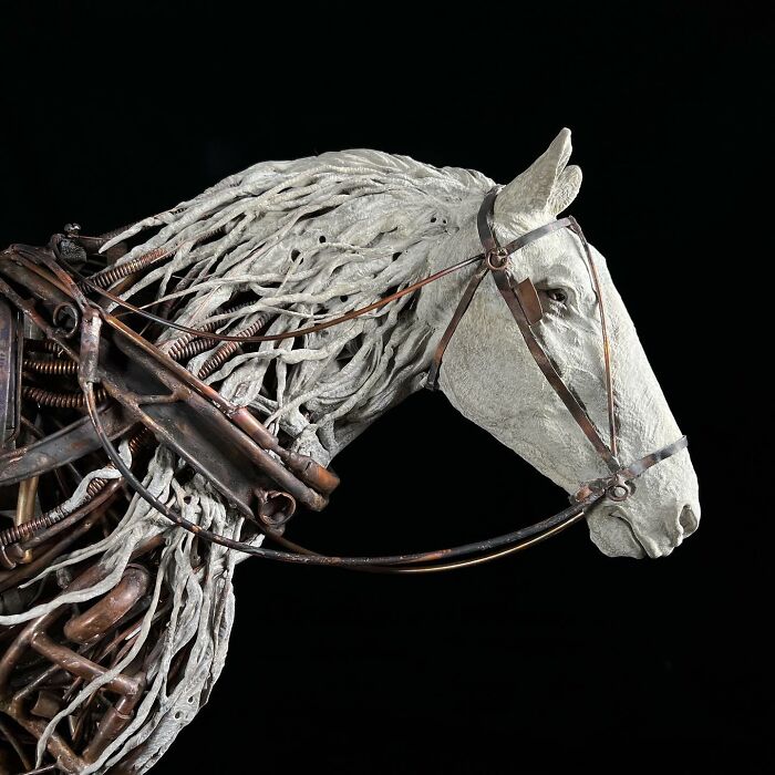 Horse sculpture made from scrap metal showcasing intricate animal sculpture details on a stone base against black background.