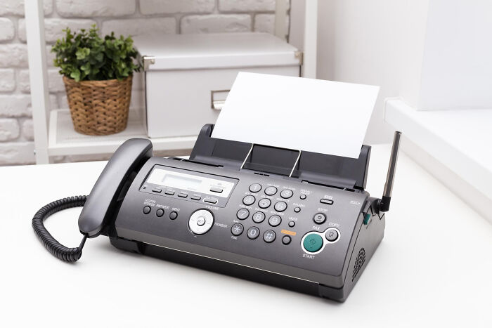 Black fax machine with handset and blank paper on a white desk, representing vintage communication from the good old days.