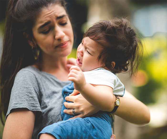 Mom holding crying toddler outdoors, expressing honest emotions about parenting challenges and backlash.