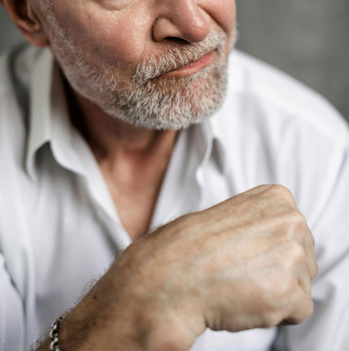 Older man with a gray beard wearing white shirt, showing frustration and waiting after message to boss following client meeting.