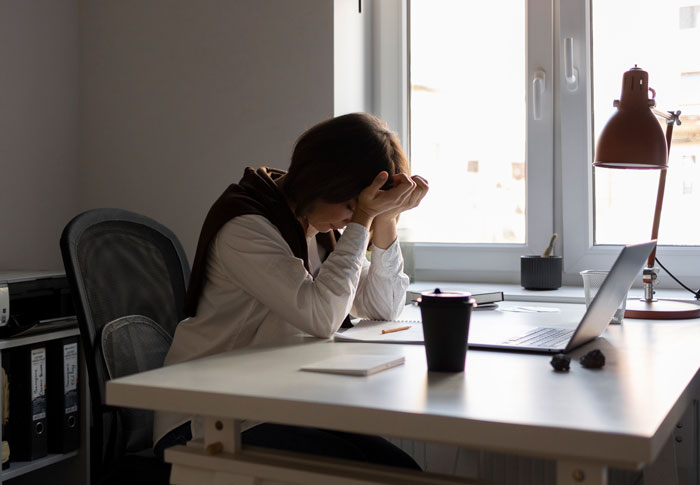 Person sitting at desk stressed with head in hands, working on laptop focused on work making reapply position. Person sitting at desk stressed with head in hands, working on laptop focused on work making reapply position.