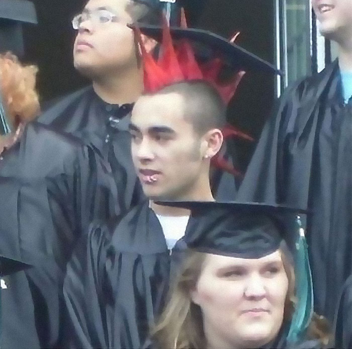 Graduates in robes with one person’s bright red spiked hair creating an awkward and painful photo moment.