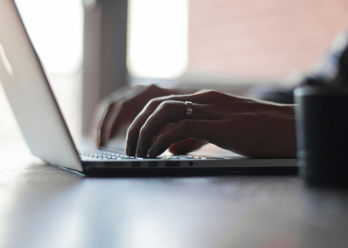 Hands typing on a laptop keyboard, illustrating a guy messaging after every client as instructed by his boss.