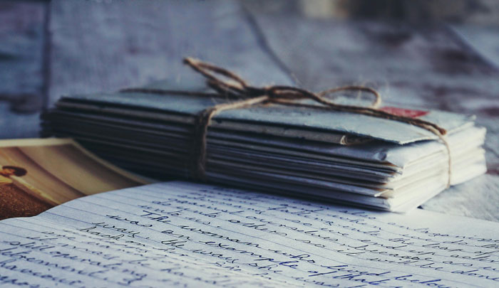 Stack of old letters tied with string on a wooden table, evoking discovery of a storage unit left in a will.