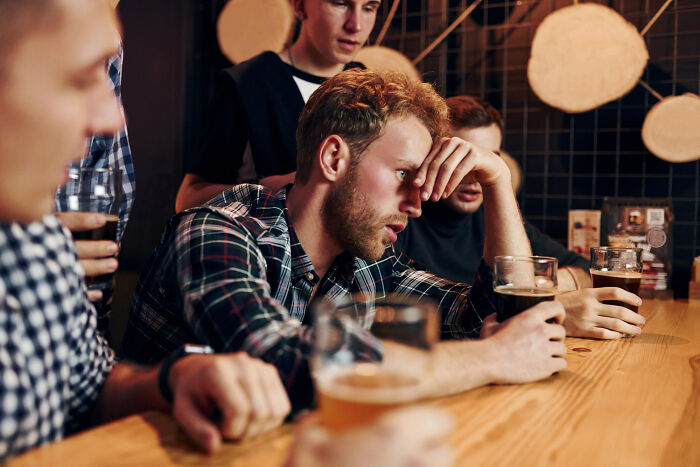 Group of young men in a bar showing wild and disgusting behavior, drinking beer and appearing exhausted or frustrated in public.