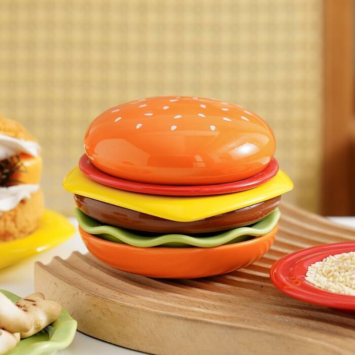 Plastic hamburger-shaped container with colorful layers, one of the weirdest picks found on Amazon displayed on a wooden board. Plastic hamburger-shaped container with colorful layers, one of the weirdest picks found on Amazon displayed on a wooden board.