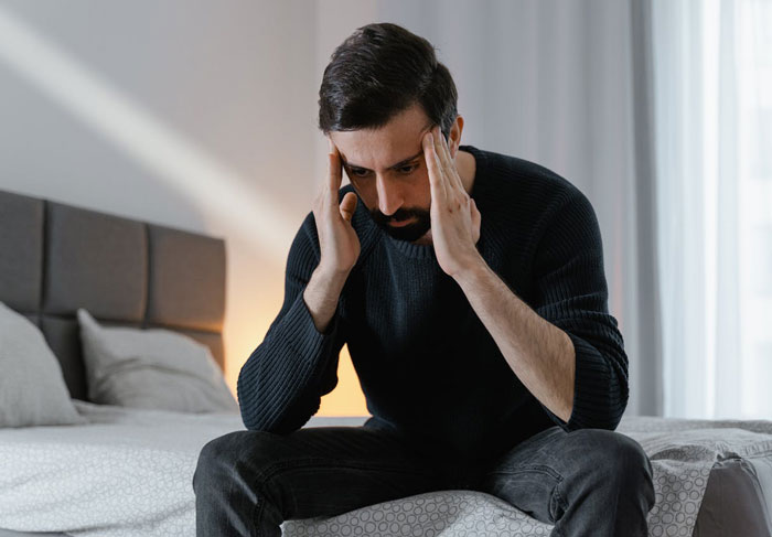 Man sitting on bed holding his head, appearing stressed or worried about menstruation celebration for daughter. Man sitting on bed holding his head, appearing stressed or worried about menstruation celebration for daughter.