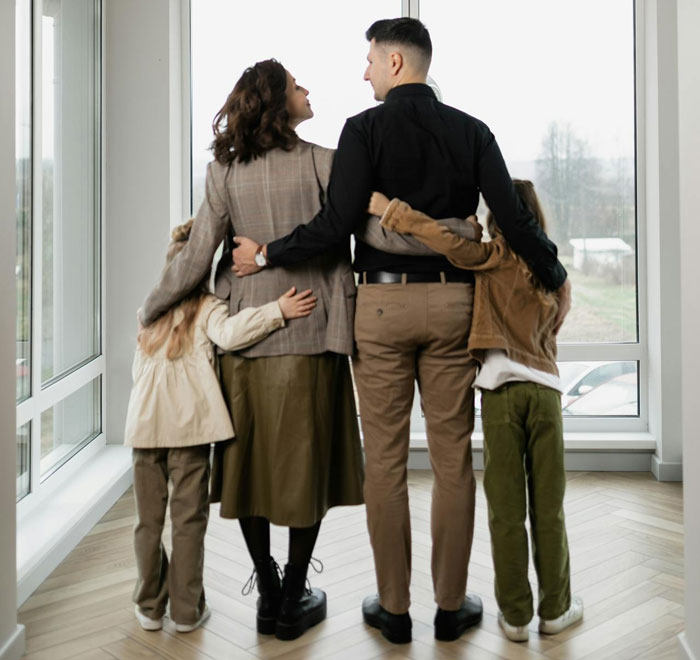 Family of four embracing near large windows, symbolizing support and a menstruation celebration for a 12-year-old daughter. Family of four embracing near large windows, symbolizing support and a menstruation celebration for a 12-year-old daughter.