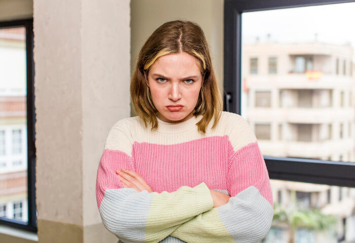 Young woman frowning with crossed arms indoors, illustrating signs netizens say reveal a couple’s days are numbered.