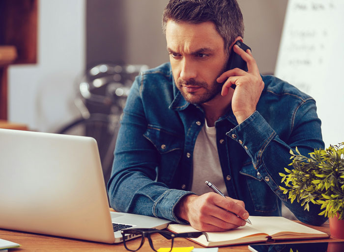 Man in denim jacket messaging after every client call, looking focused and ignored for three hours while working at desk.