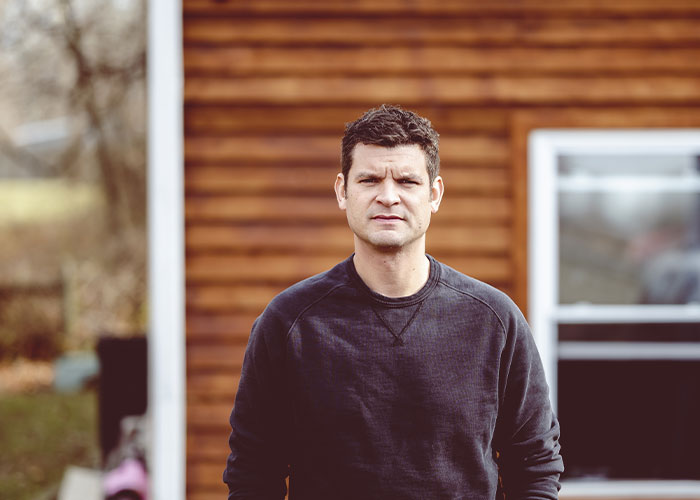 Man standing outside a house, looking serious, representing tension in a relationship after a red-flag argument. Man standing outside a house, looking serious, representing tension in a relationship after a red-flag argument.