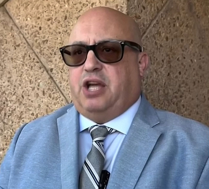 Man wearing sunglasses and a suit speaking outside court about baby lost in car while mom got lip filler charges