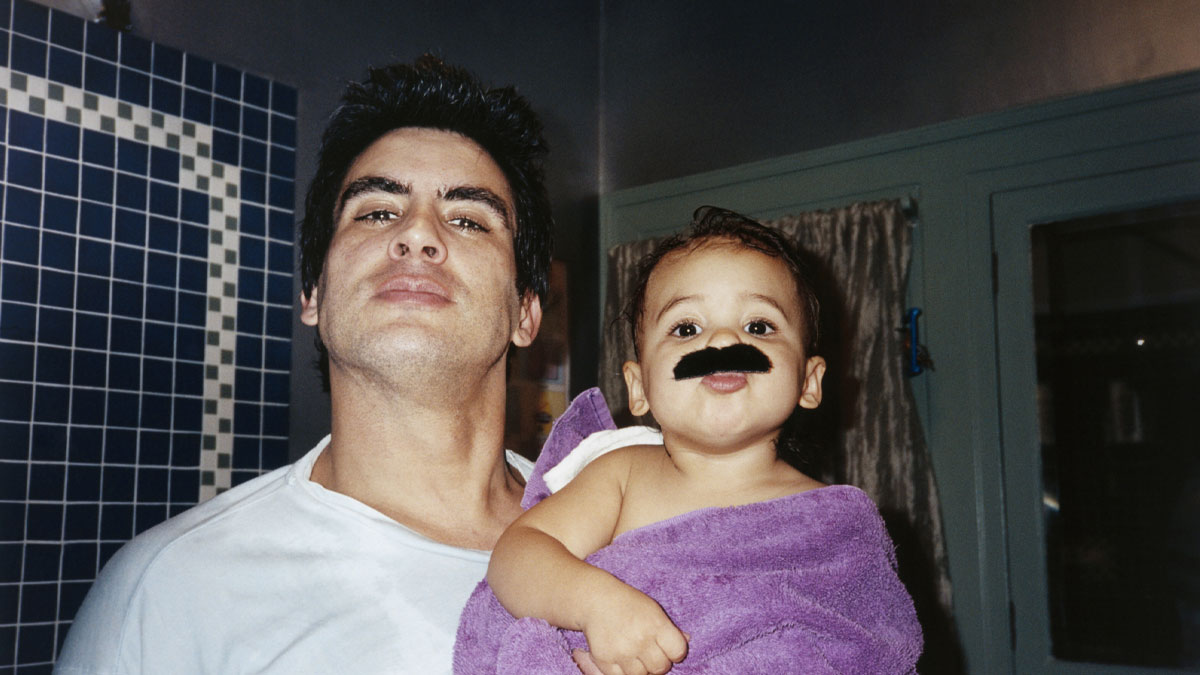 Father holding baby boy wrapped in purple towel with a fake mustache, representing rare boy names for stand-out babies.