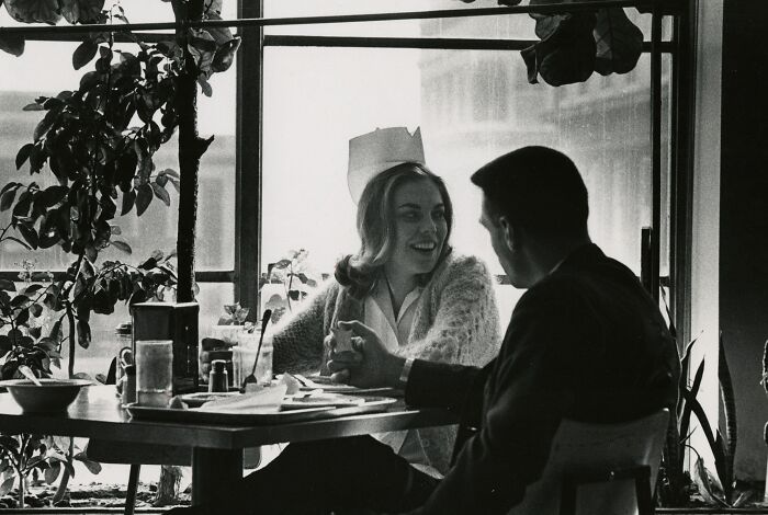 Vintage photo of a nurse smiling and talking to a man at a table, showcasing classic nursing and healing moments.