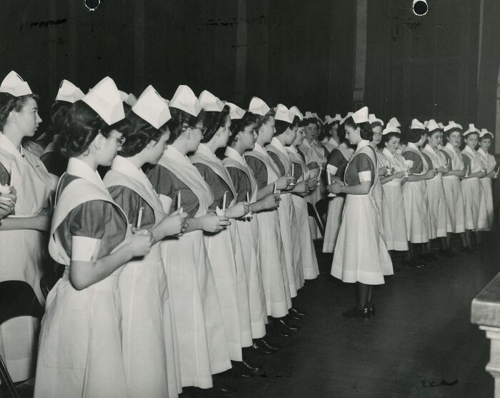 Vintage nurses in uniform holding candles during a ceremonial event, showcasing healing and hope in a historic setting.