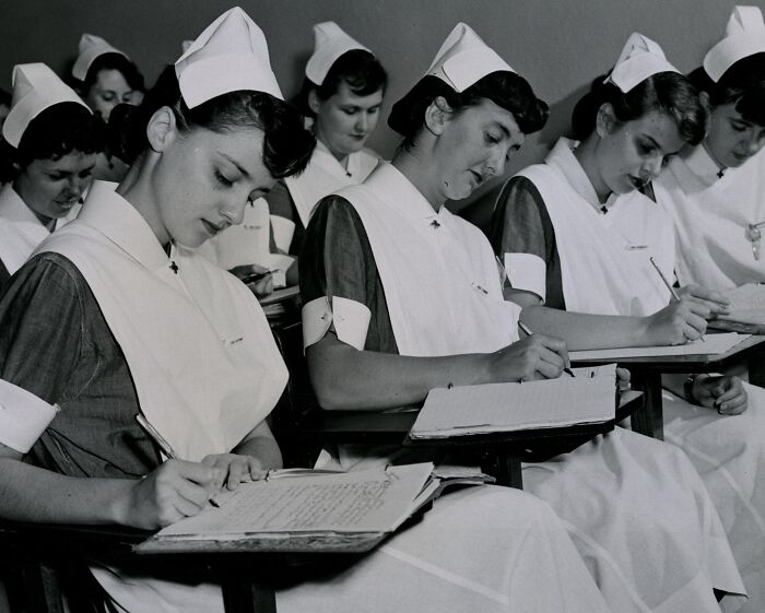 Vintage nurses in traditional uniforms writing notes in a classroom, highlighting the dedication of vintage nurses in healthcare history.