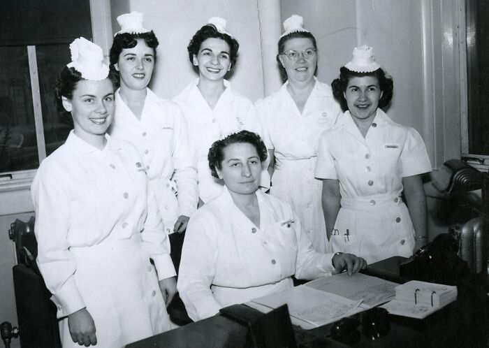 Group of vintage nurses in classic uniforms gathered around a desk, showcasing healing and hope from past decades.