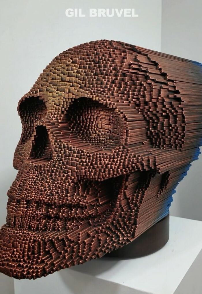 Wooden sticks sculpted into a detailed 3D skull face with hypnotic texture and depth on a white pedestal.