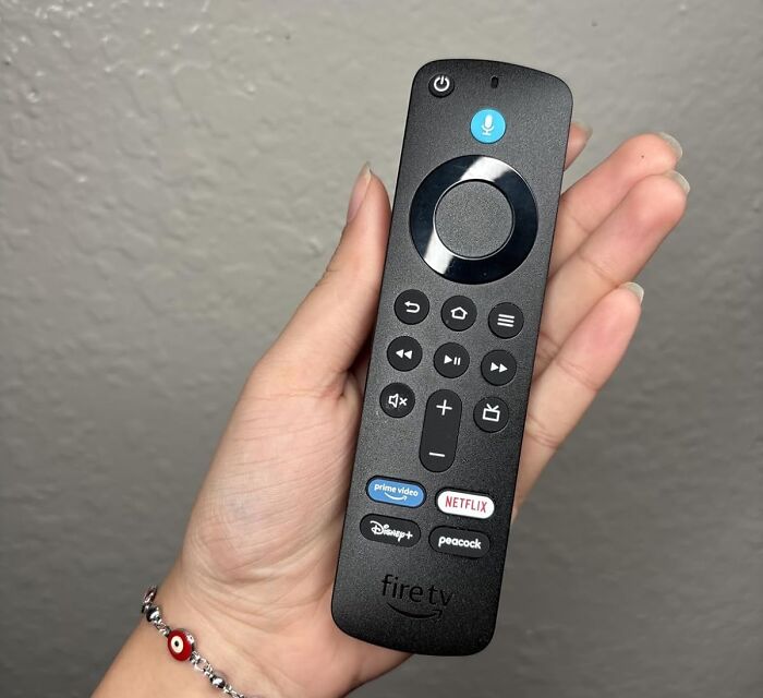 Hand holding a Fire TV remote featuring streaming app buttons, highlighting Prime Day electronic deals and add to cart options.