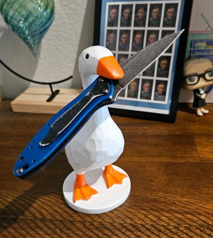 White duck figurine holding a blue folding knife, showcasing fun home decor on a wooden surface with background items.