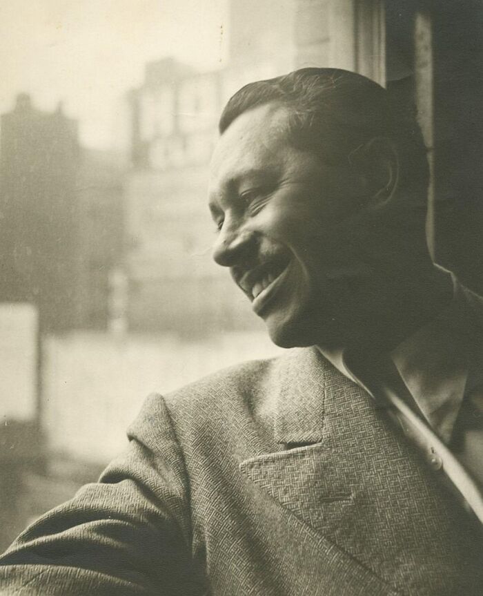 Smiling man in a vintage 1930s suit near window, evoking the charm of 1930s vintage postcards and timeless style.