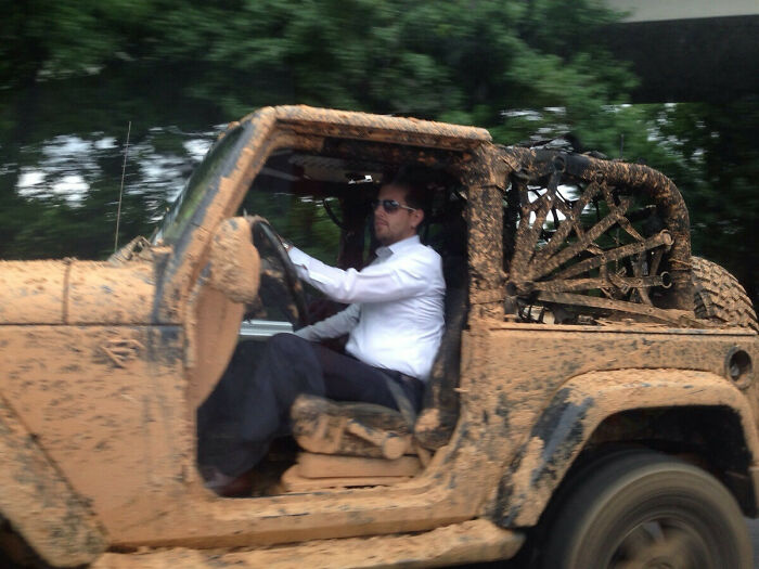 Man in white shirt driving a muddy off-road vehicle, looking suspiciously unbothered by the messy surroundings.