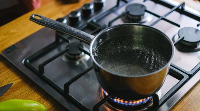 Black saucepan boiling water on gas stove flame, illustrating general science knowledge question about boiling point in Celsius.