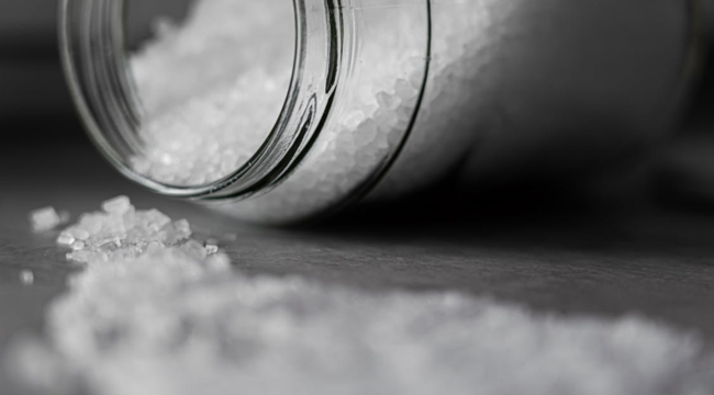 Close-up of coarse table salt crystals spilled from a glass container, illustrating general science knowledge and chemistry concepts.