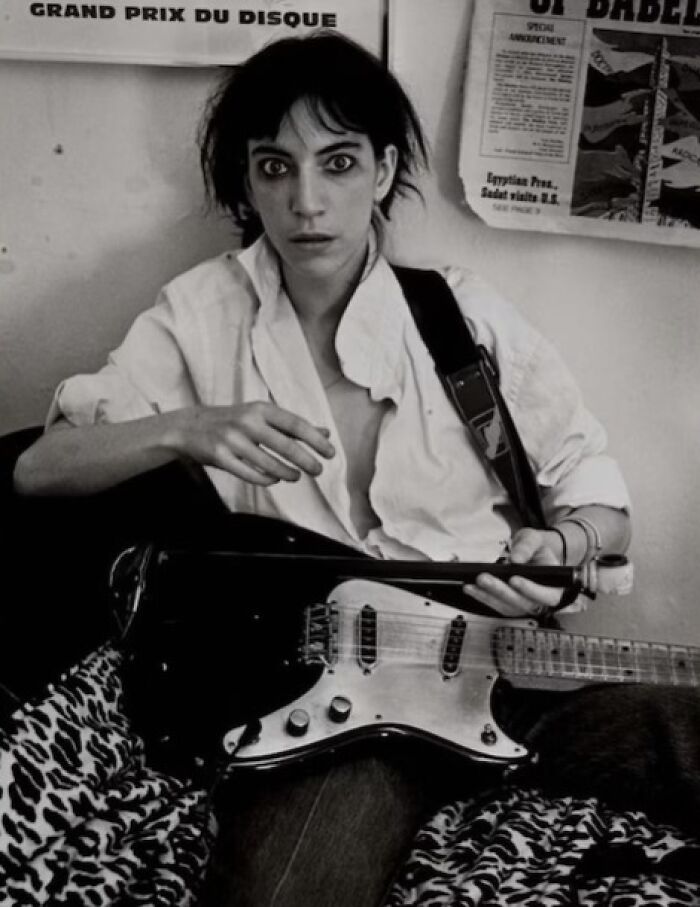 1970s rock legend in a raw studio moment, holding electric guitar and wearing a white shirt in black and white photo.