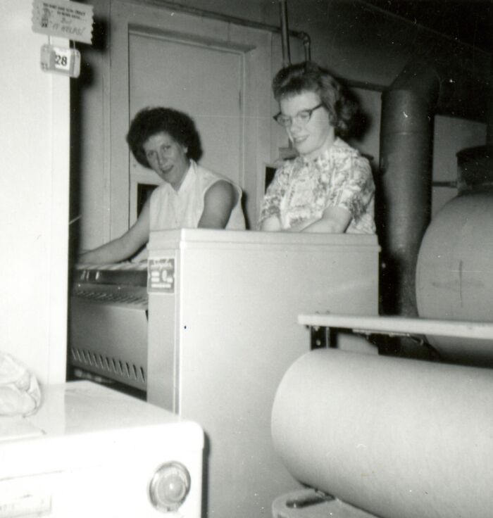 Two women using industrial laundry machines, showcasing daily life across the globe in the 50s in a black and white photo.