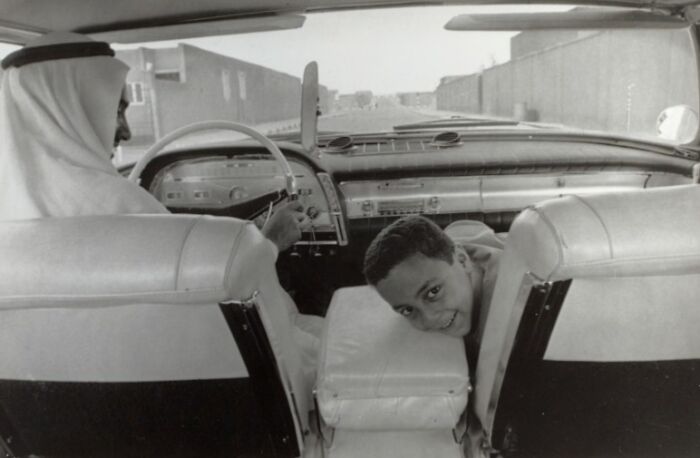 Black and white photo of a man and boy in a car, capturing daily life across the globe in the 50s era.