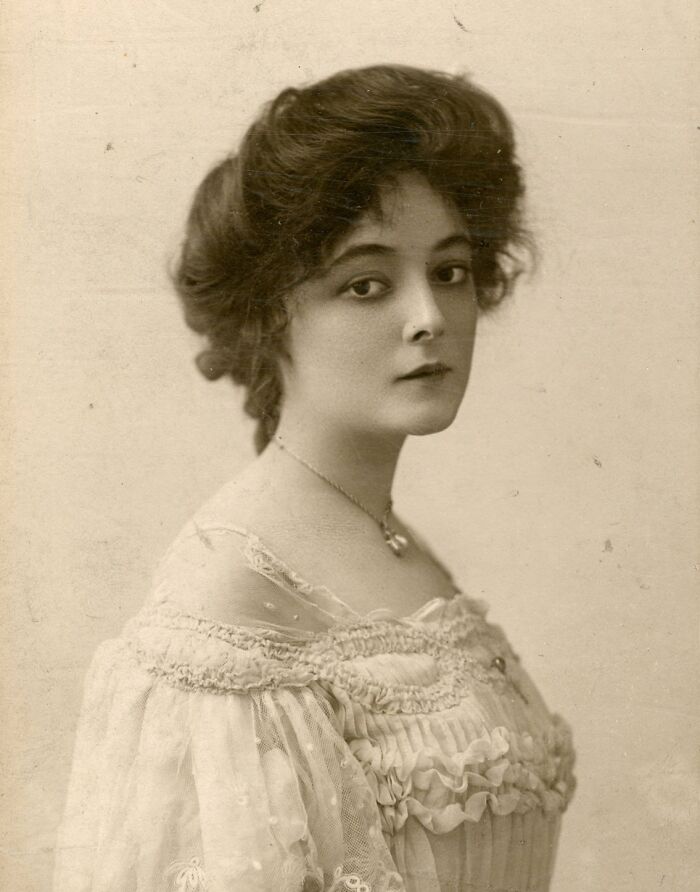 Vintage sepia photo of a woman with timeless beauty in an elegant off-shoulder ruffled dress, early 20th century style.