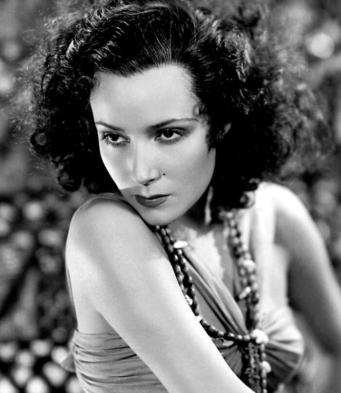 Black and white century-old photo of a woman with curly hair and beads, representing timeless beauty and classic elegance.