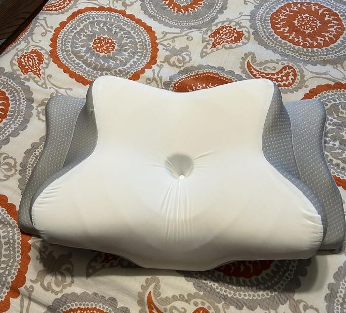 Ergonomic white and gray pillow with contoured support on patterned bedding, highlighting under-the-radar find for comfort.