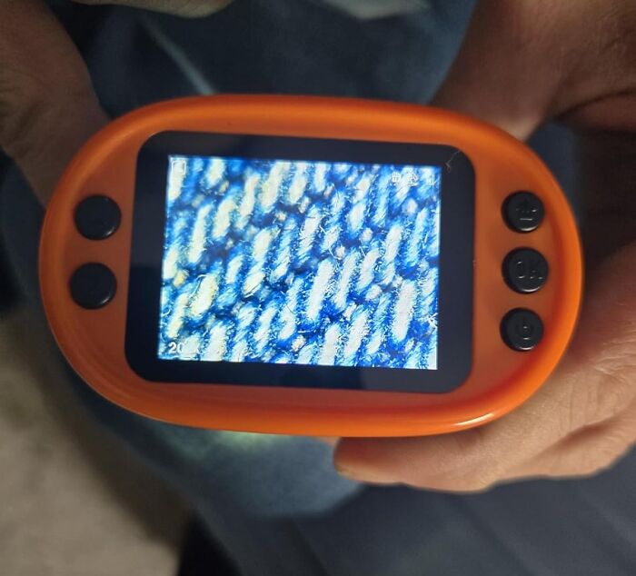 Hand holding an orange digital microscope showing a close-up textured surface, highlighting under-the-radar finds clearly.