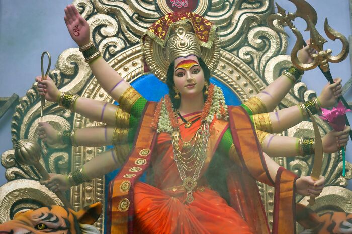 Statue of a multi-armed goddess in a vibrant orange and green outfit symbolizing religious myths and beliefs.