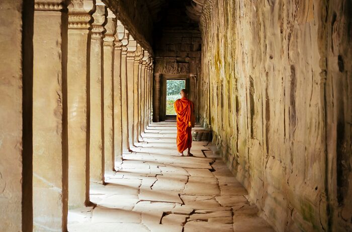 A monk in orange robes walking in an ancient stone corridor symbolic of religious myths and biblical history.