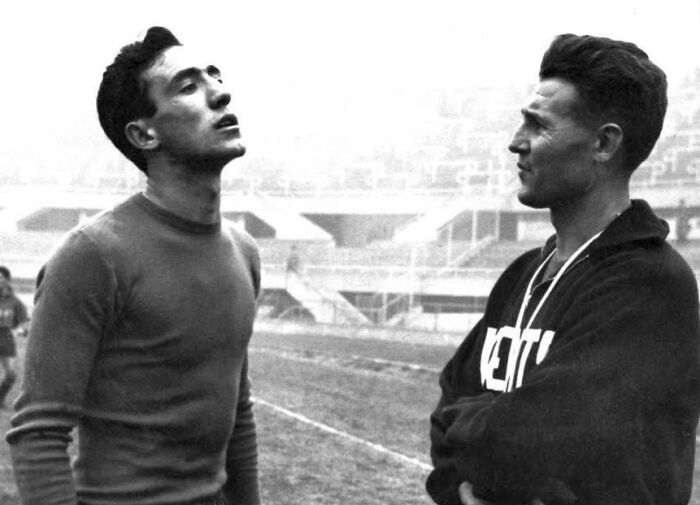 Two men in 1950s sportswear having a conversation on a stadium field, capturing daily life across the globe in the 50s.