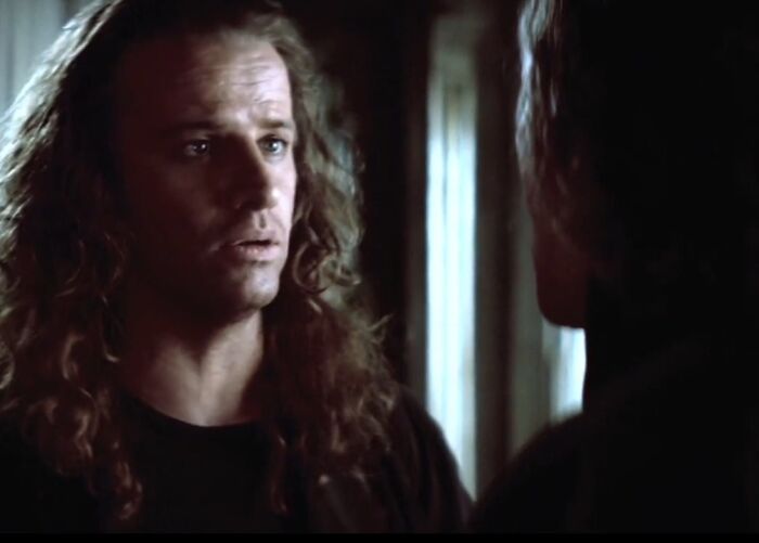 Scene from a cinematic crime movie sequel featuring a serious face-off between two characters in a dimly lit room.