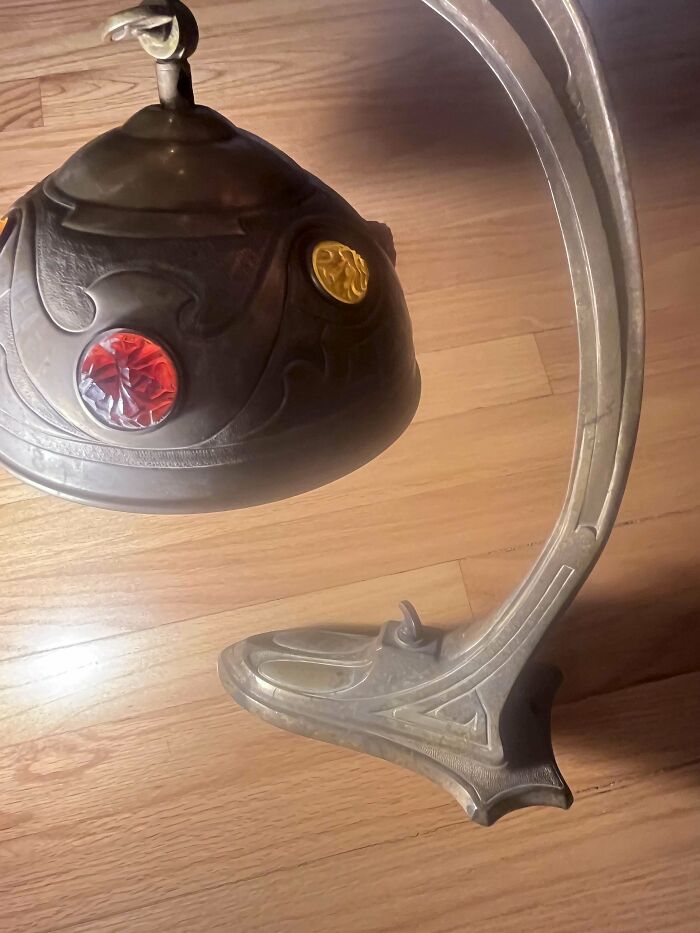 Vintage metal lamp with decorative red and yellow glass accents on a curved ornate base on wooden floor, old things.