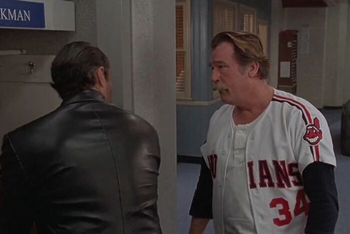 Two men in a hallway, one in a Cleveland Indians baseball jersey, depicting a scene from cinematic crimes in movie sequels.