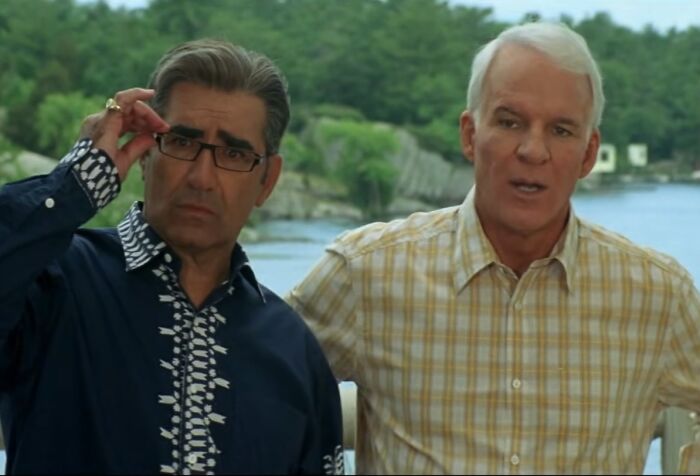 Two men by a lake, one adjusting glasses, representing cinematic crimes in the worst movie sequels of all time.