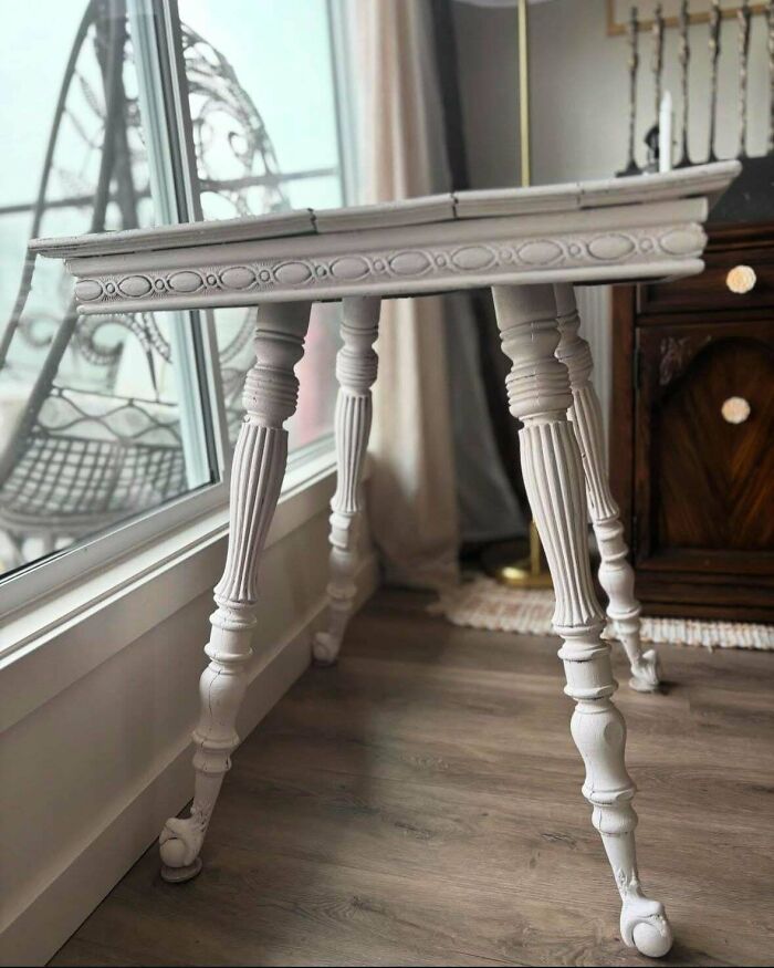 Ornate vintage wooden table with carved legs standing on hardwood floor near window, showcasing beautiful old things.