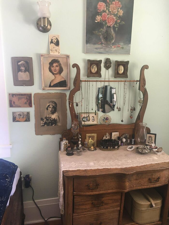 Vintage wooden vanity with old framed portraits, delicate jewelry, and antique decor in a cozy room setting.